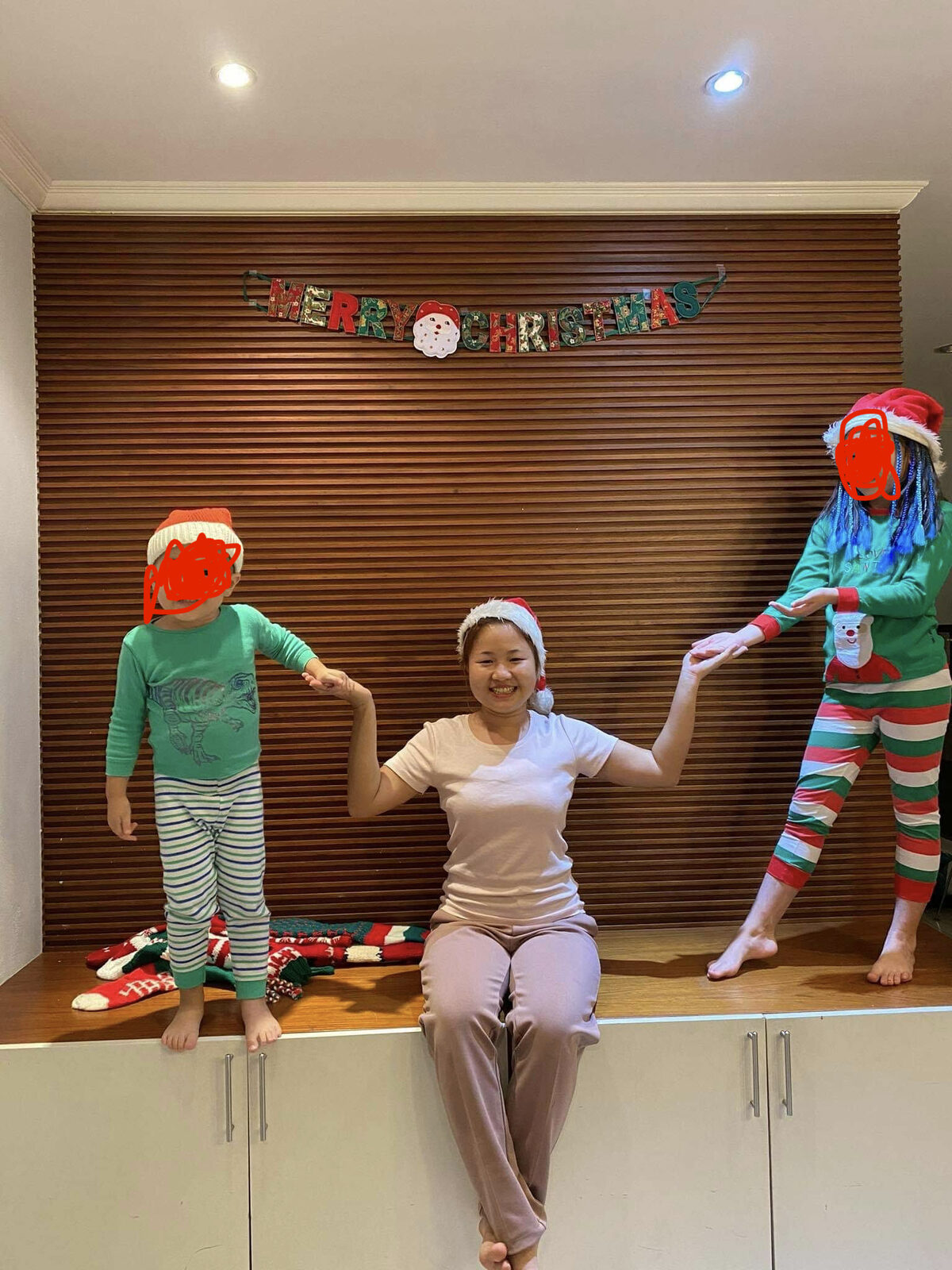 Our nanny in a Santa hat with my two kids in Christmas pyjamas at our home in Bangkok